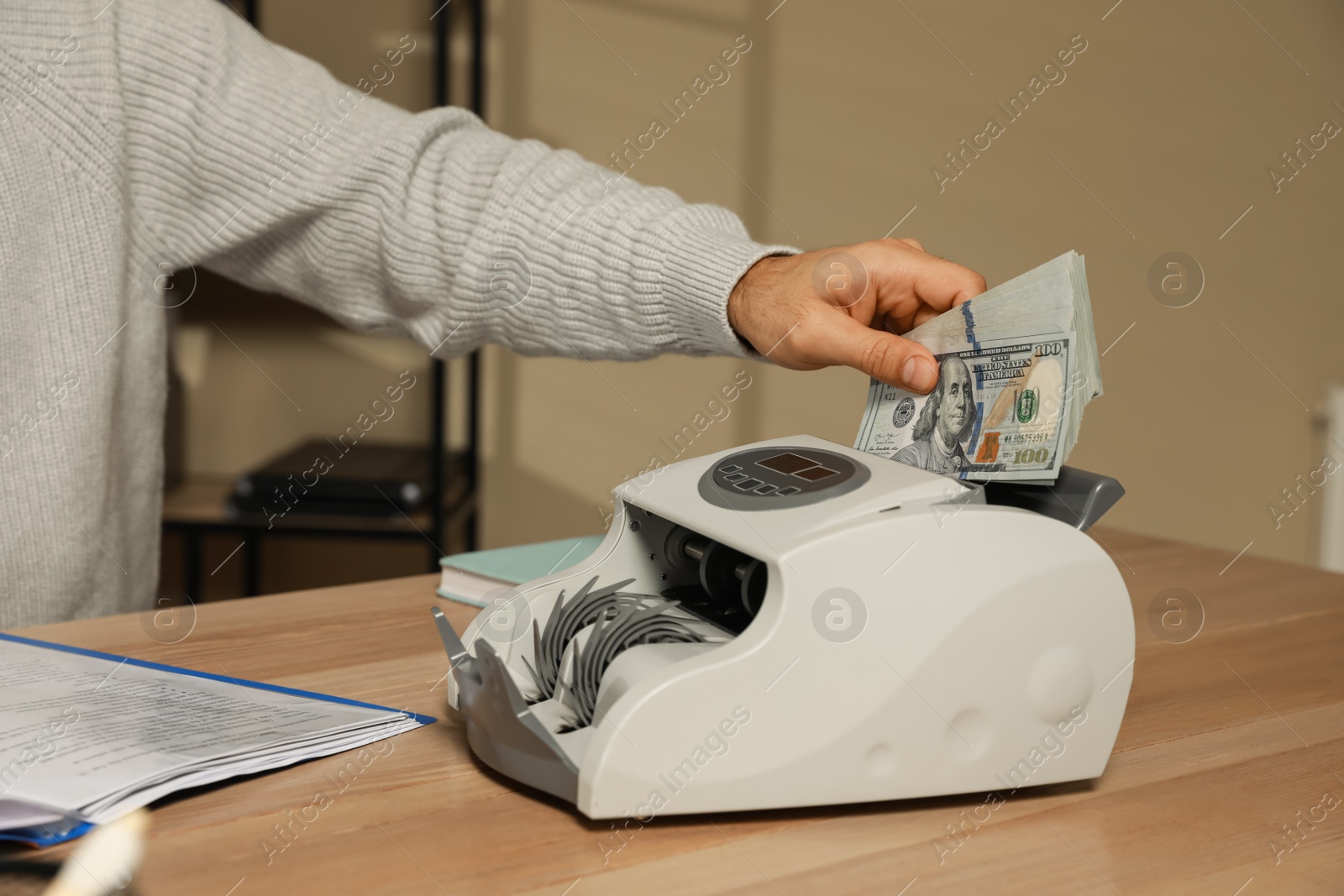 Photo of Man putting money into banknote counter at wooden table indoors, closeup