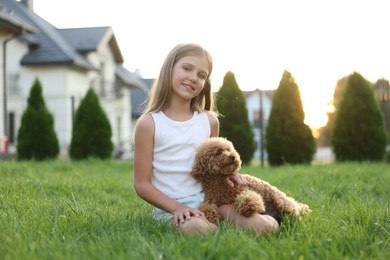 Photo of Beautiful girl with cute Maltipoo dog on green lawn in backyard