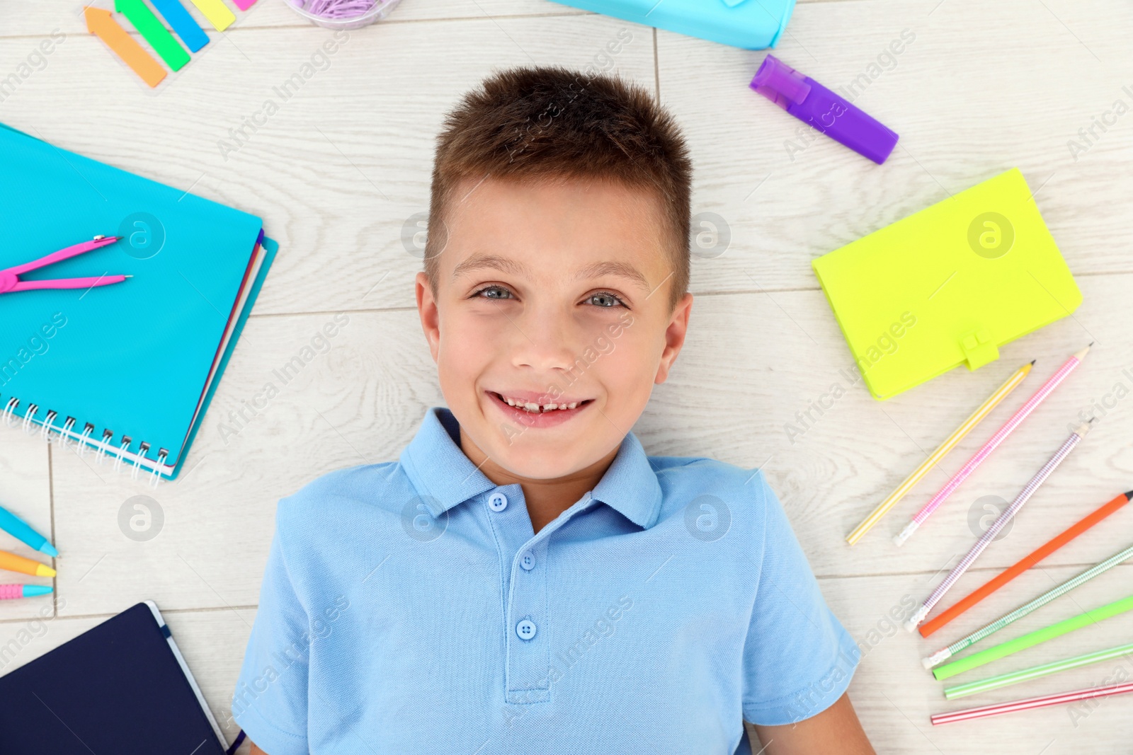 Photo of Cute little boy with school stationery on wooden background, top view