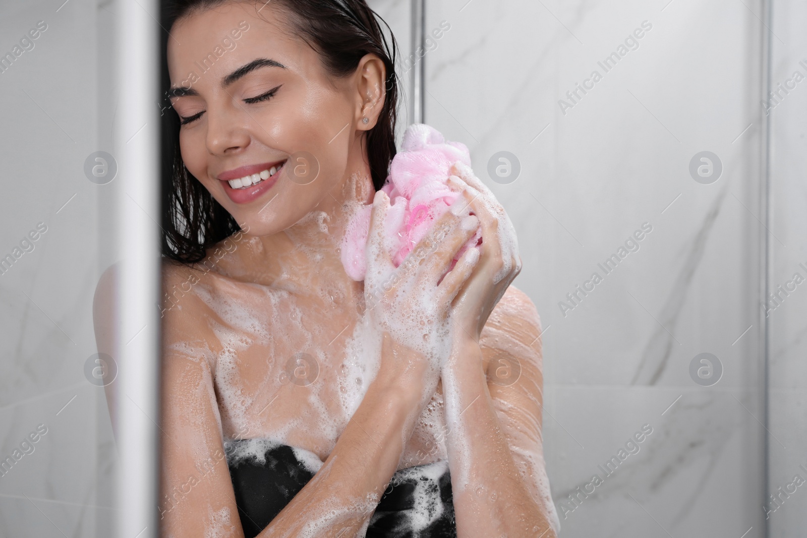 Photo of Young woman with mesh pouf taking shower at home