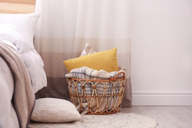 Photo of Basket with blanket and pillows near bed indoors