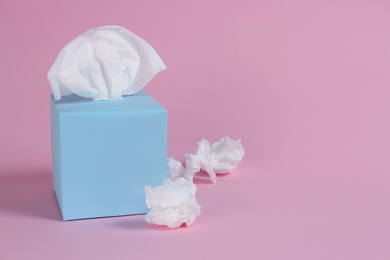 Photo of Box with paper tissues and used crumpled napkins on pink background, space for text