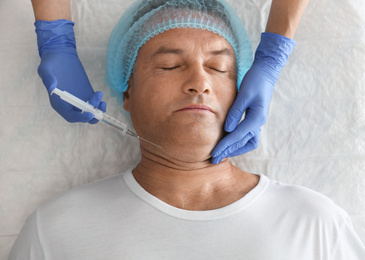 Photo of Mature man with double chin receiving injection in clinic, above view