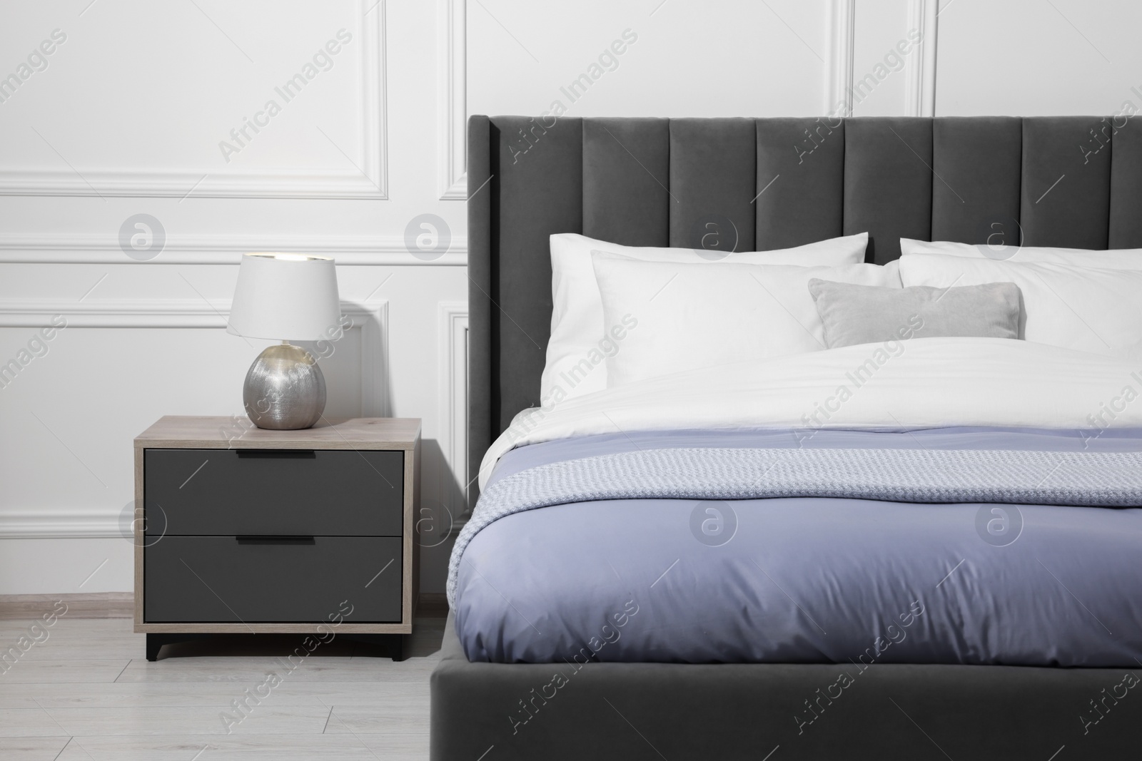 Photo of Comfortable bed near bedside table with lamp in stylish bedroom