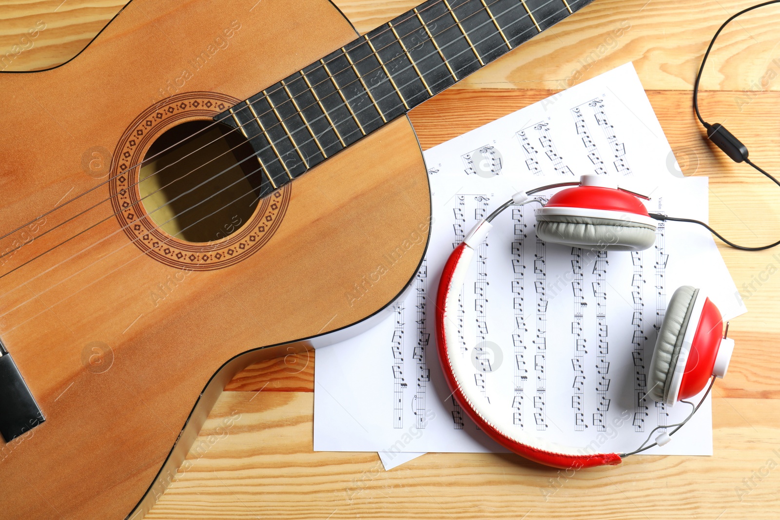 Photo of Beautiful classical guitar, headphones and music sheets on wooden background, top view