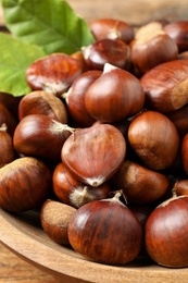 Photo of Fresh sweet edible chestnuts in wooden bowl, closeup
