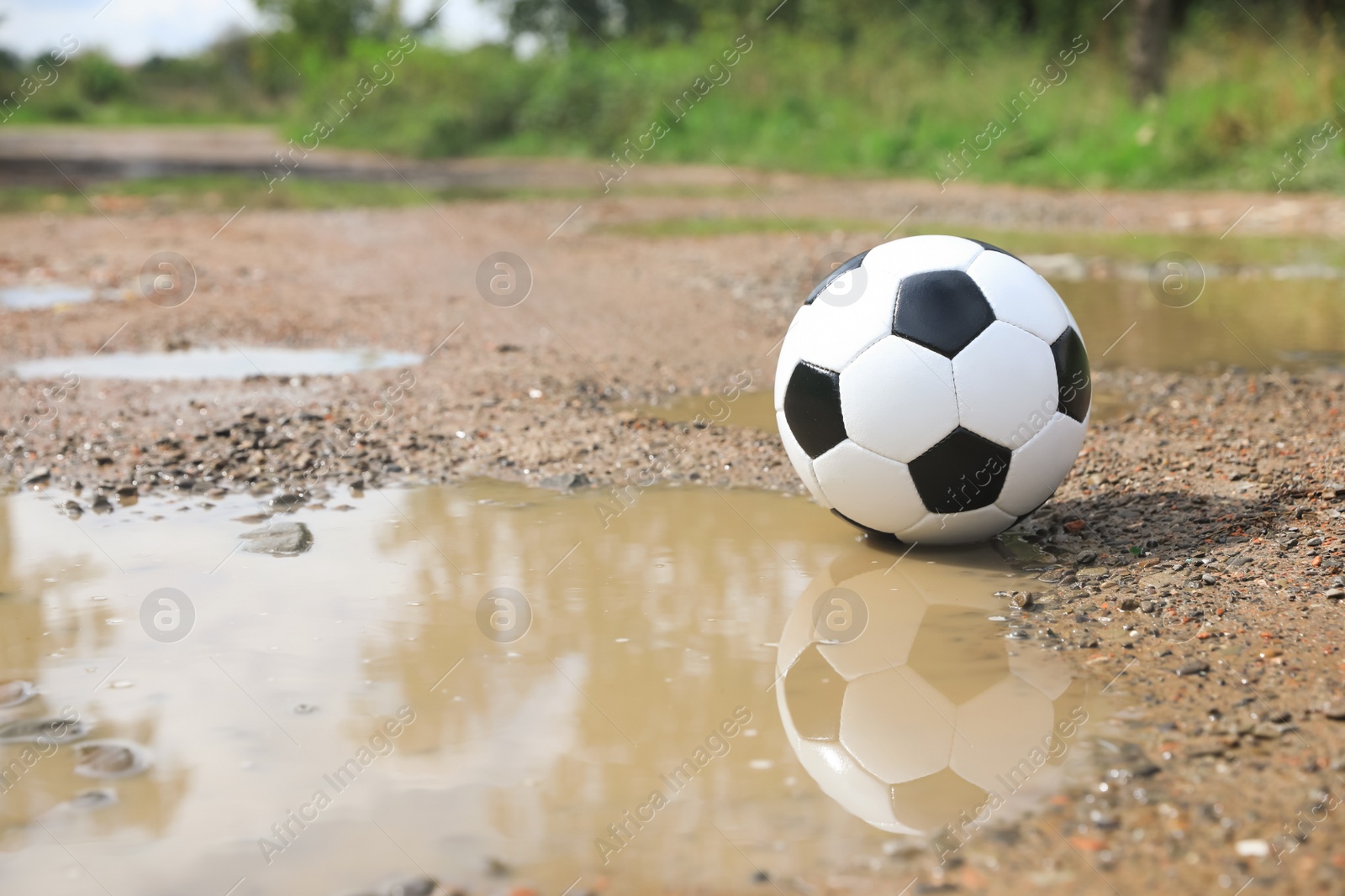 Photo of Soccer ball near puddle outdoors, space for text