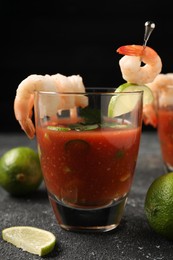 Photo of Tasty shrimp cocktail with sauce in glasses and limes on grey textured table against black background, closeup