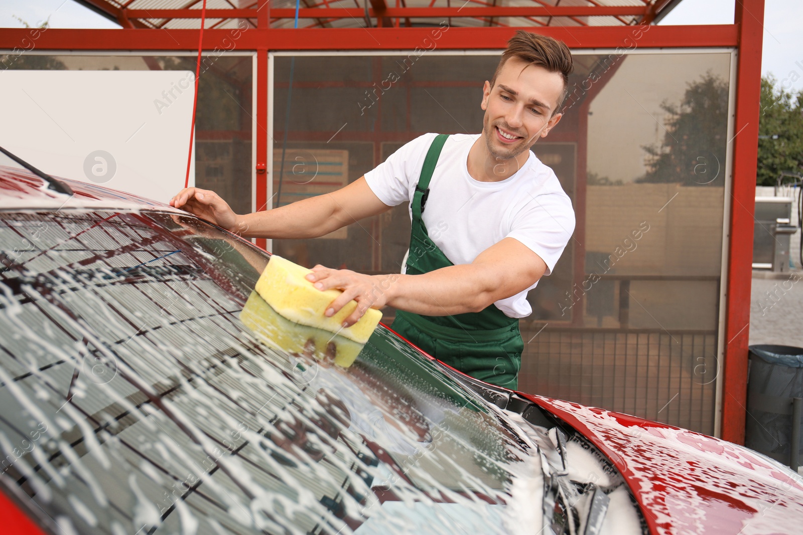 Photo of Male worker cleaning vehicle with sponge at car wash