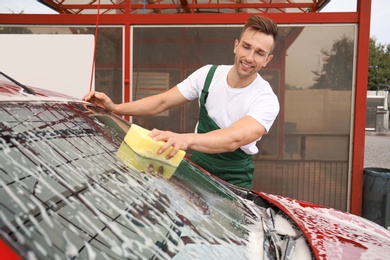 Male worker cleaning vehicle with sponge at car wash