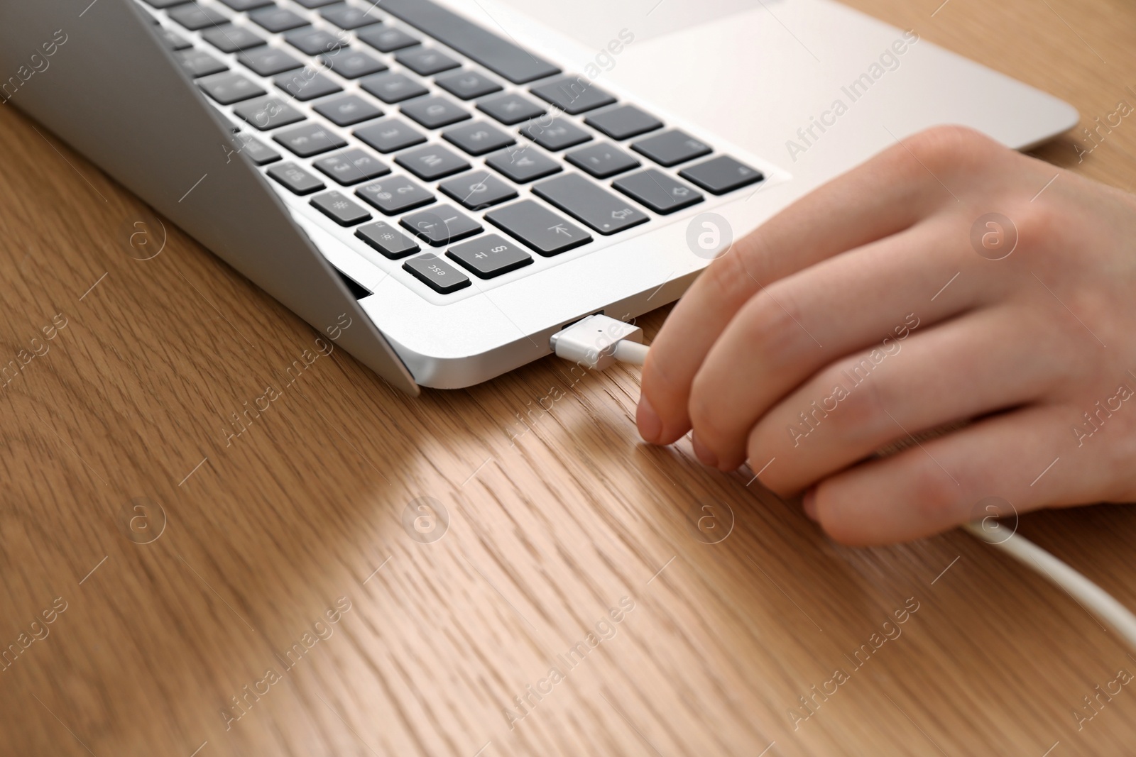 Photo of Woman connecting charging cable to laptop at wooden table, closeup