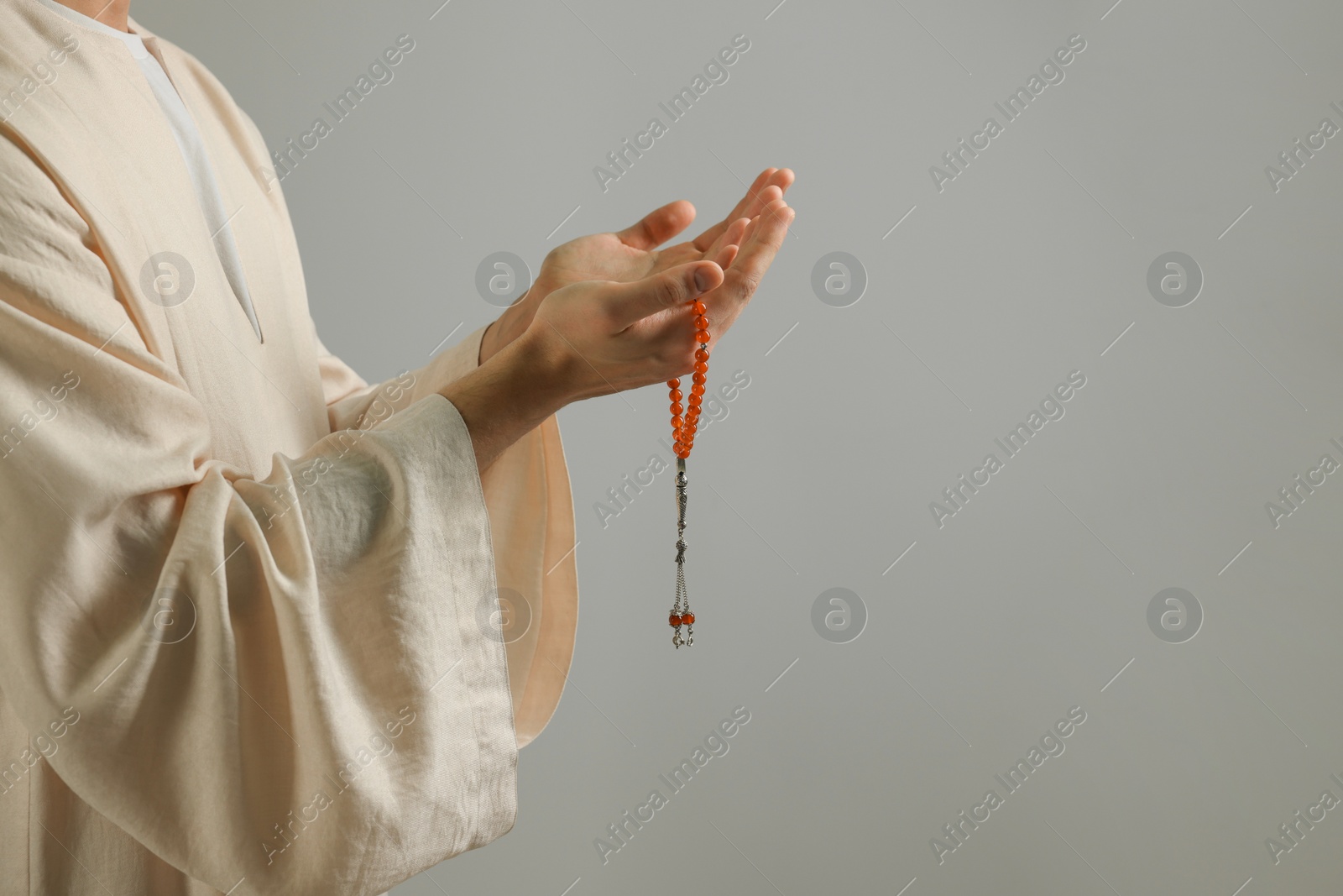 Photo of Muslim man with misbaha praying on light grey background, closeup. Space for text