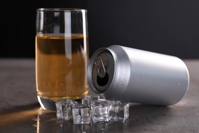 Photo of Energy drink in glass, aluminium can and ice cubes on grey table, closeup