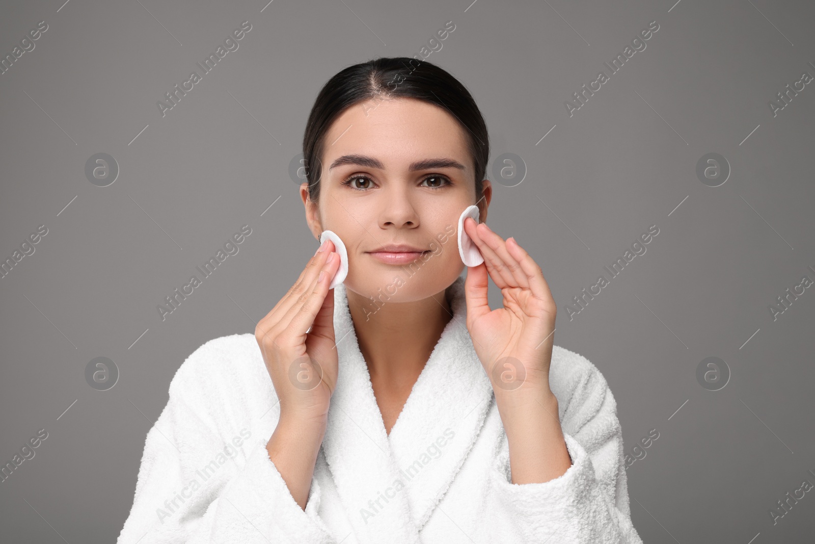 Photo of Young woman cleaning her face with cotton pads on grey background