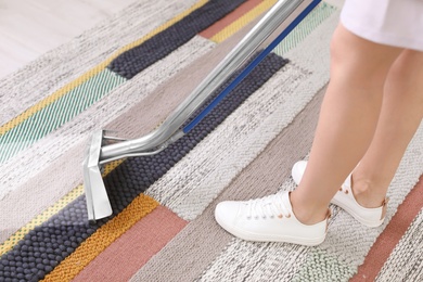 Female worker removing dirt from carpet with professional vacuum cleaner indoors