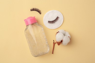 Photo of Bottle of makeup remover, cotton flower, pad and false eyelashes on yellow background, flat lay