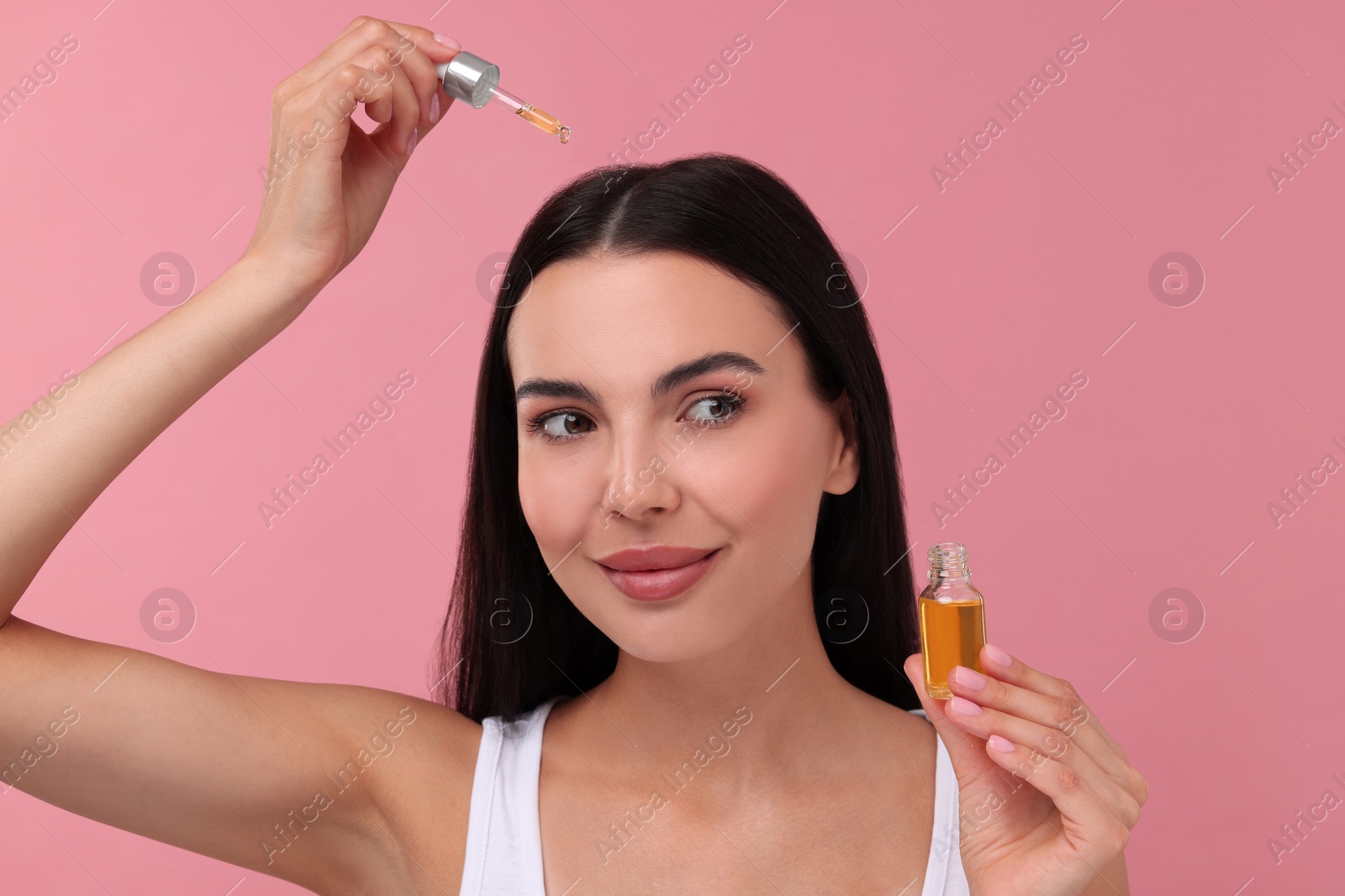 Photo of Beautiful woman applying hair serum on pink background. Cosmetic product