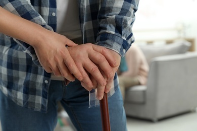 Photo of Nurse assisting elderly man with cane indoors, closeup. Space for text