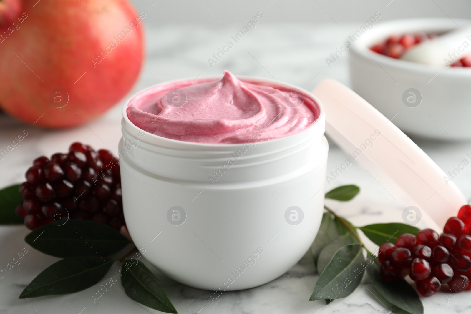 Photo of Fresh pomegranate and jar of facial mask on white marble table, closeup. Natural organic cosmetics