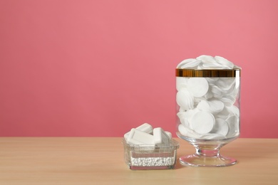 Photo of Jar with cotton pads on wooden table against pink background. Space for text