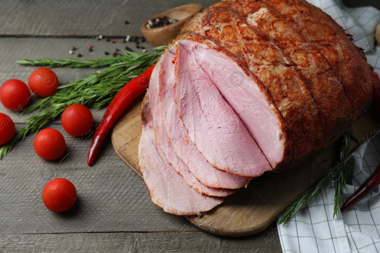 Photo of Delicious baked ham, tomatoes, chili pepper and rosemary on grey wooden table, closeup