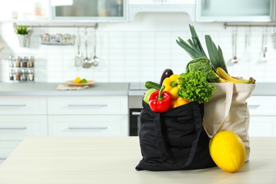 Textile shopping bags full of vegetables and fruits on table in kitchen. Space for text