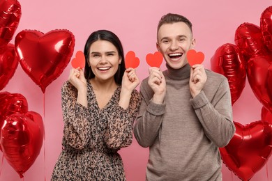 Photo of Lovely couple with decorative hearts near balloons on pink background