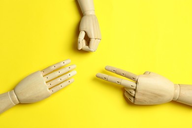 Photo of Wooden mannequin hands on yellow background, flat lay