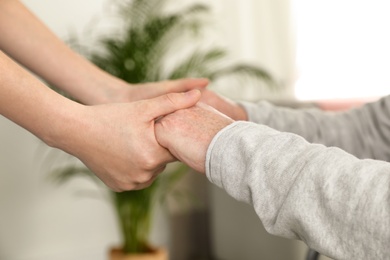 Photo of Nurse holding elderly man's hands indoors, closeup. Assisting senior people