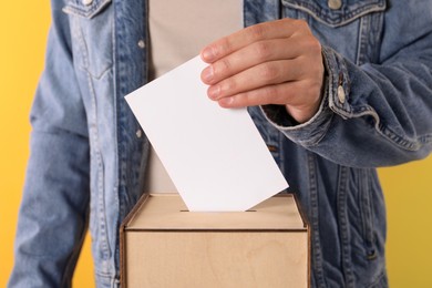 Photo of Man putting his vote into ballot box on yellow background, closeup