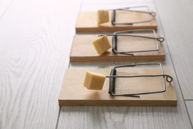 Photo of Mousetraps with pieces of cheese on white wooden background. Pest control
