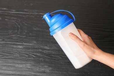 Woman with bottle of protein shake on wooden background, top view. Space for text