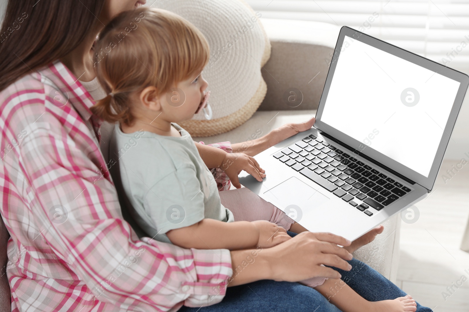 Photo of Mother and daughter with laptop on sofa at home. Pediatrician online consultation