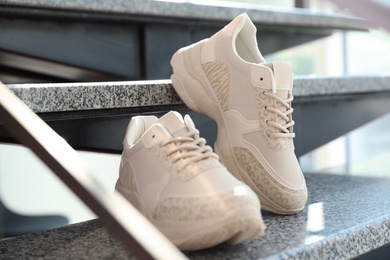 Photo of Pair of stylish women's sneakers on grey marble stairs indoors