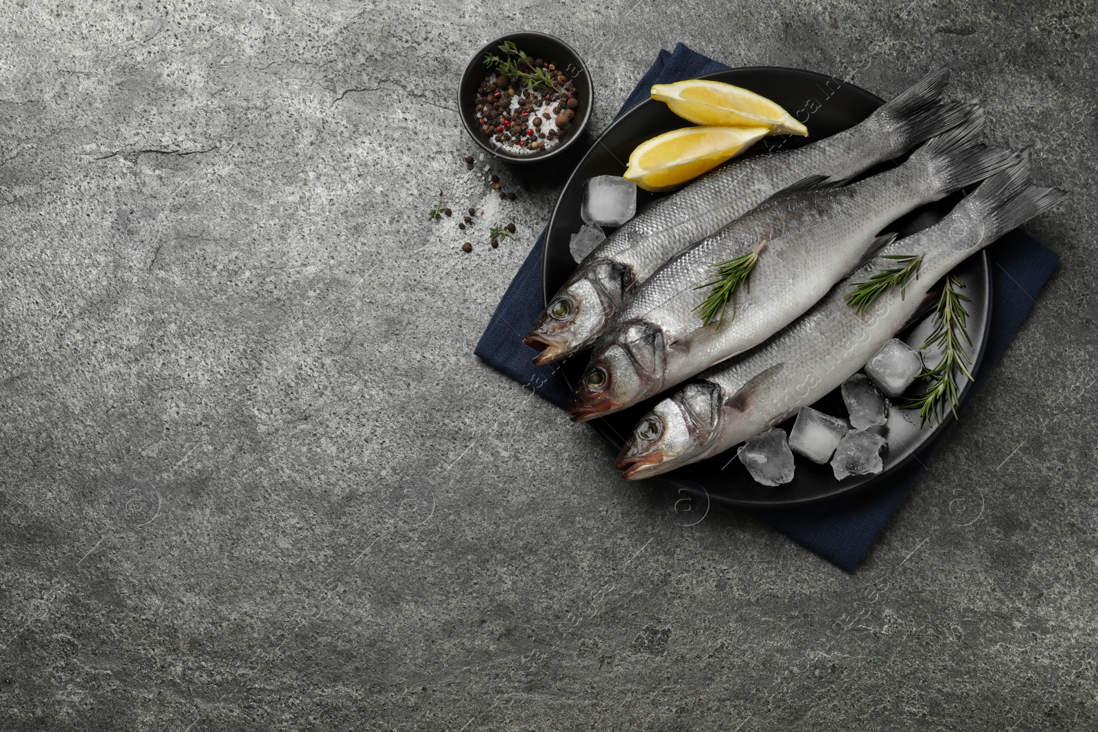 Photo of Sea bass fish and ingredients on grey table, flat lay. Space for text