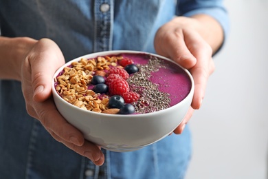 Photo of Woman holding bowl of acai smoothie with granola and berries, closeup