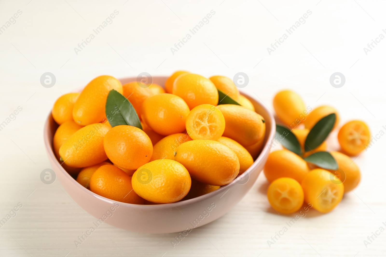 Photo of Fresh ripe kumquats with green leaves on white wooden table