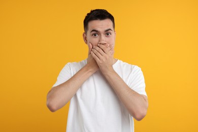 Photo of Embarrassed man covering mouth with hands on orange background