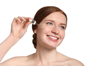 Photo of Smiling woman with freckles applying cosmetic serum onto her face on white background