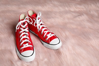 Photo of Pair of stylish red sneakers on faux fur rug. Space for text