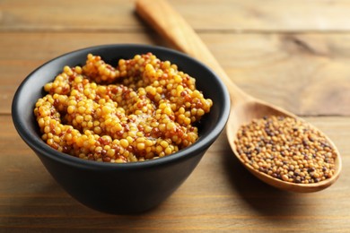 Photo of Whole grain mustard in bowl and dry seeds on wooden table, closeup