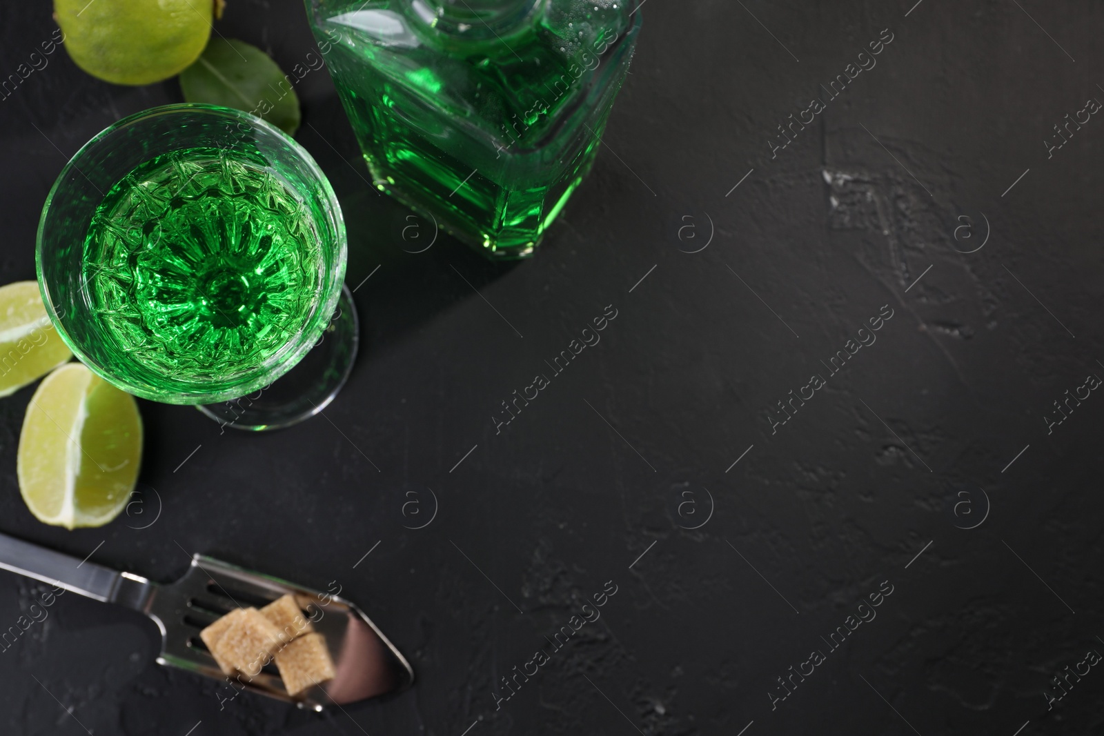 Photo of Absinthe, spoon, brown sugar and lime on black table, flat lay with space for text. Alcoholic drink