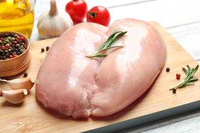 Photo of Wooden board with raw chicken breasts and ingredients on table, closeup