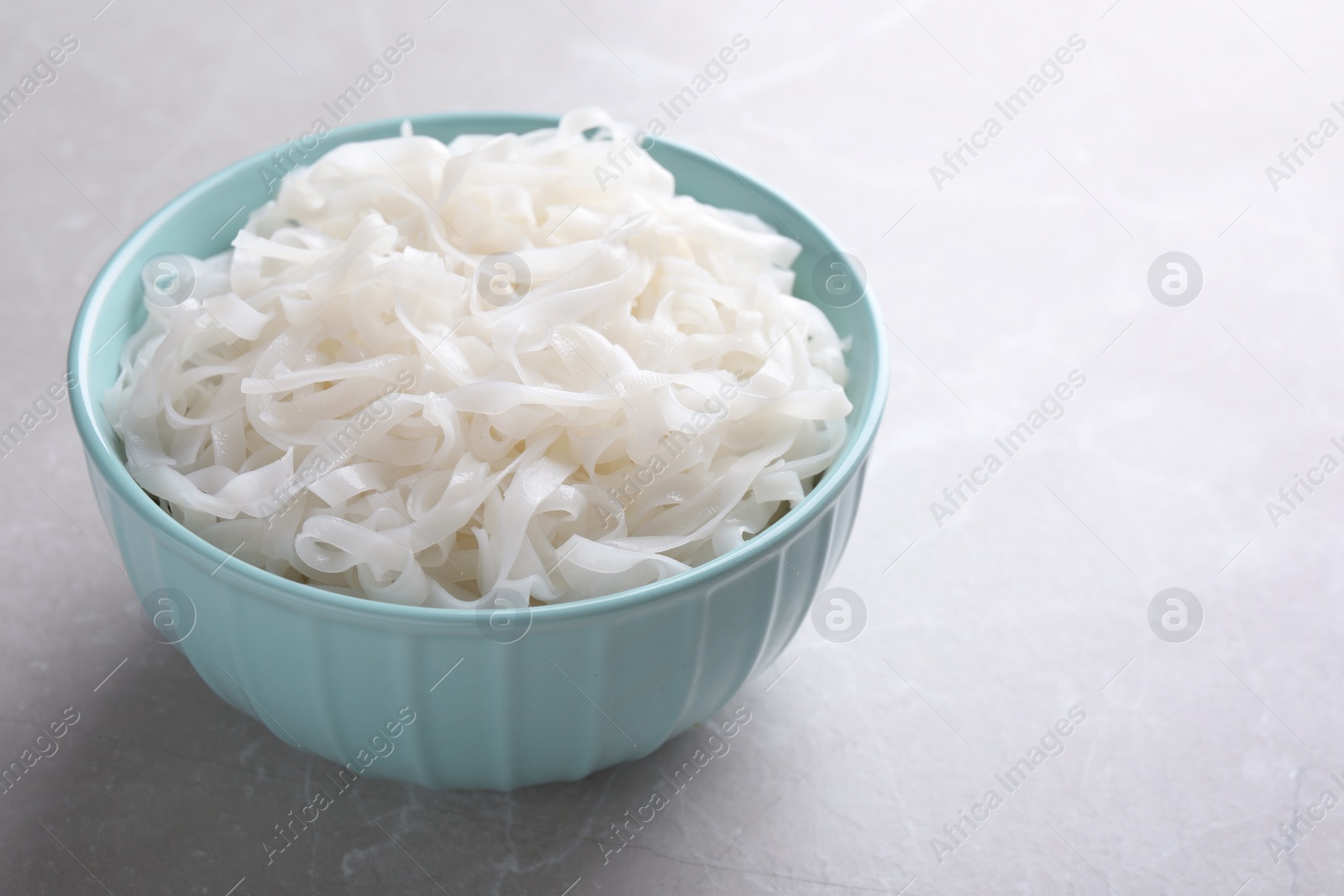 Photo of Bowl of tasty cooked rice noodles on light grey table. Space for text