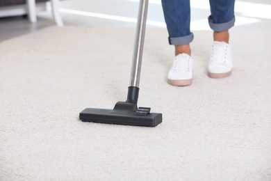 Photo of Woman cleaning carpet with vacuum cleaner, closeup
