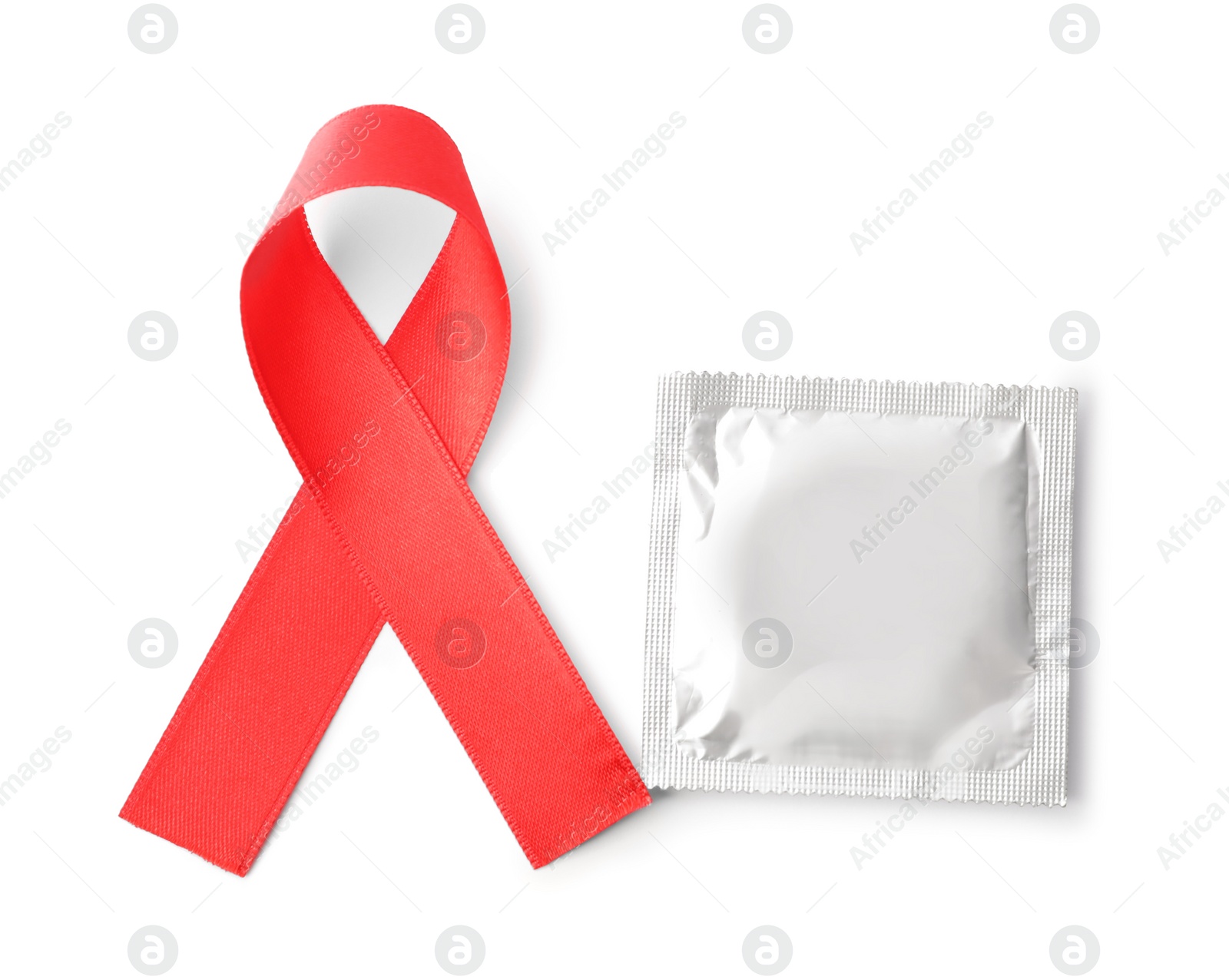 Photo of Red ribbon and condom isolated on white, top view. AIDS disease awareness