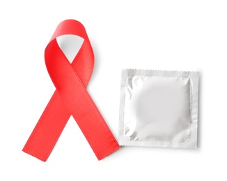 Photo of Red ribbon and condom isolated on white, top view. AIDS disease awareness