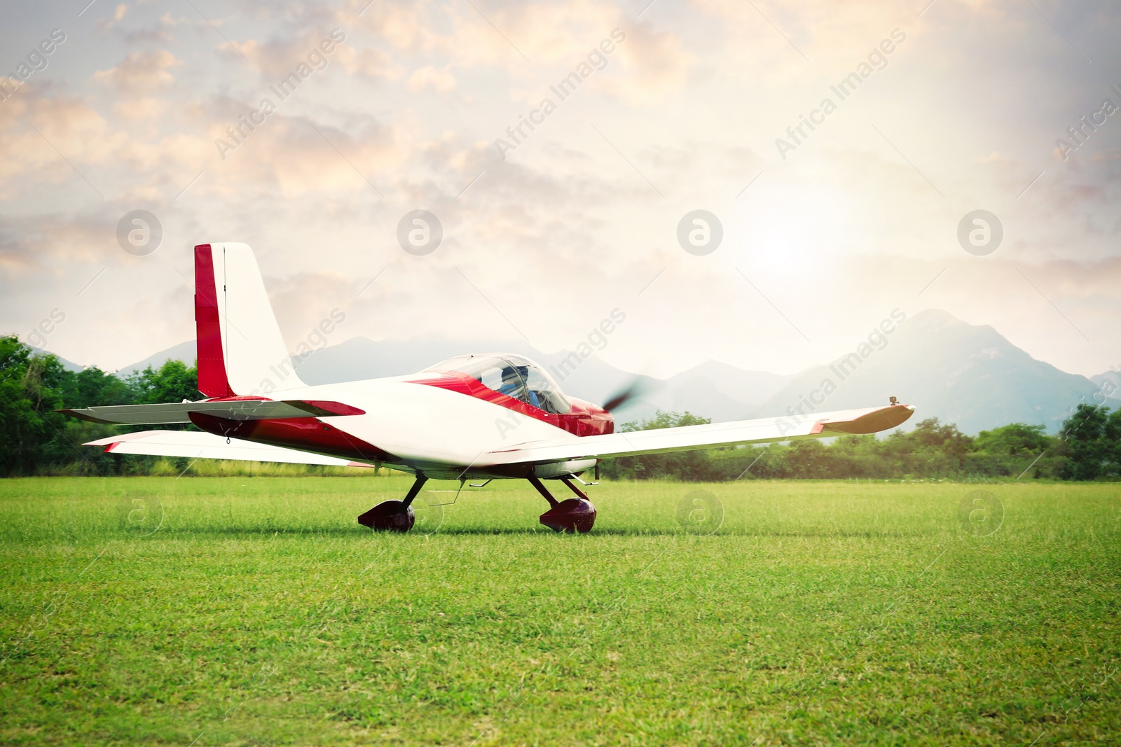 Photo of Ultralight aircraft on green grass near trees and mountains