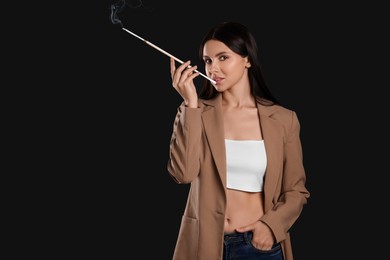 Woman using long cigarette holder for smoking on black background, space for text