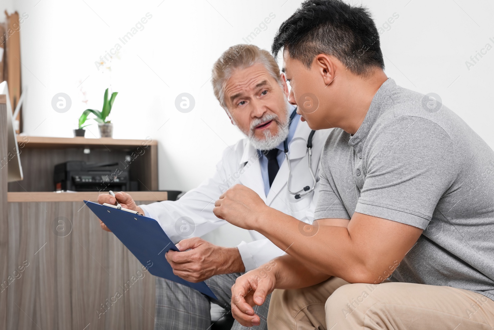 Photo of Senior doctor with clipboard consulting patient in clinic